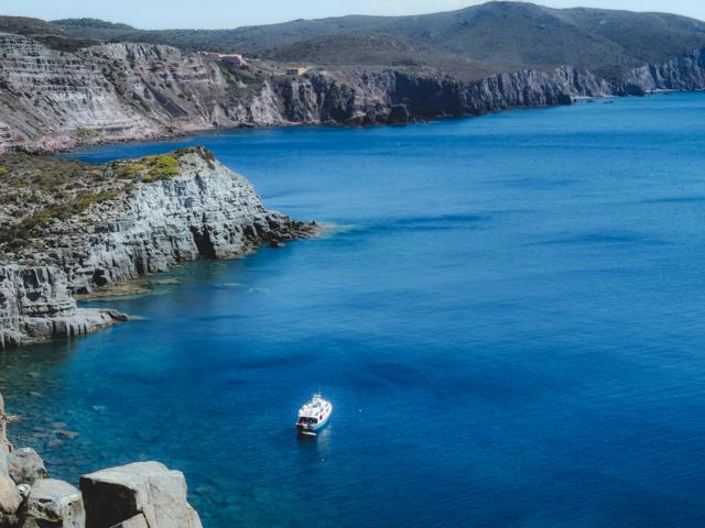 Felsen, Meer und Boote an der Cala Fico Sardinien thealkamalsontheroad